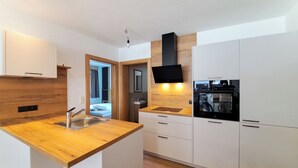 A modern kitchen with a wooden countertop, stainless steel sink, and white cabinetry. - Apartment Tyrol by Interhome (Auffach)
