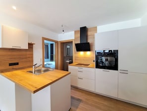 A modern kitchen with a wooden countertop, stainless steel sink, and white cabinetry. - Apartment Tyrol by Interhome (Auffach)