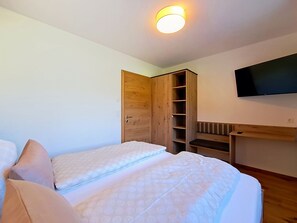 A bedroom with two beds, a wooden wardrobe, a TV mounted on the wall, and a bench with cushions. - Bavaria by Interhome (Auffach)