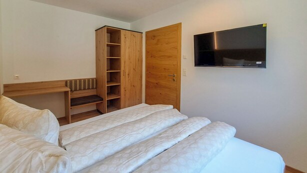 A bedroom with a bed, a wooden wardrobe, a television mounted on the wall, and a bedside table. - Apartment Tyrol by Interhome (Auffach)