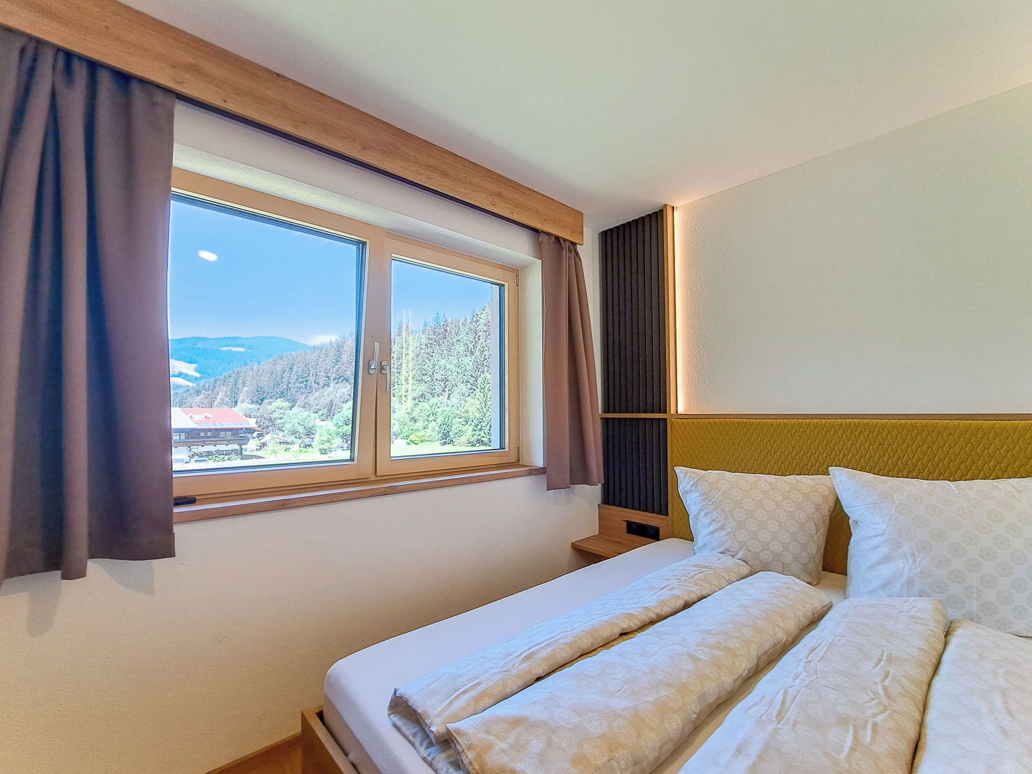 Une chambre d’hôtel avec un lit, une fenêtre avec des rideaux et une vue sur une zone boisée.