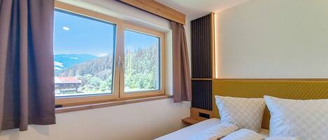 Une chambre d’hôtel avec un lit, une fenêtre avec des rideaux et une vue sur une zone boisée.