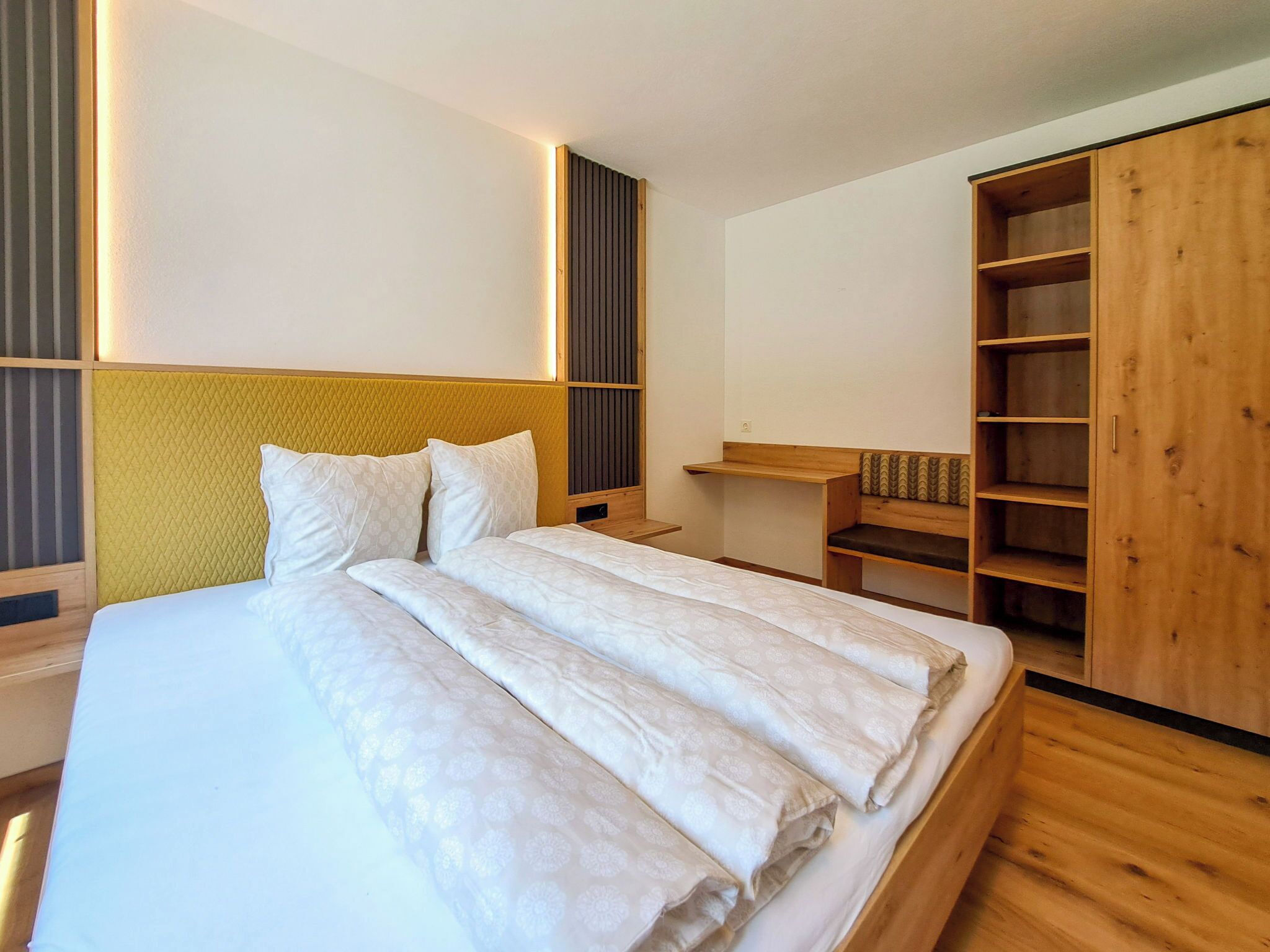 Une chambre moderne avec un grand lit, une tête de lit en bois, des étagères intégrées et une armoire.