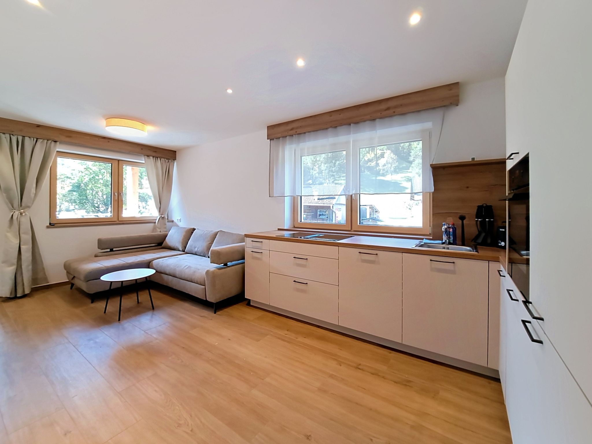 Eine moderne Küche mit Backofen, ein Essbereich mit einer Couch und einem kleinen Tisch sowie ein Fenster mit Vorhängen.