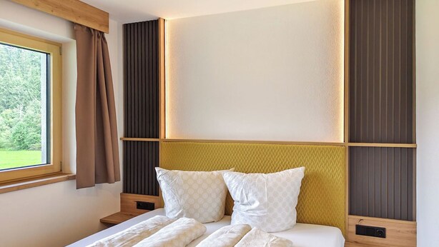 Quarto moderno com cama grande, janela com cortinas e vista para o verde lá fora.