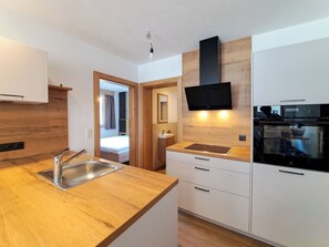 Eine moderne Küche mit Holzarbeitsplatten, einem eingebauten Ofen und einem flachbildschirmigen Fernseher an der Wand.