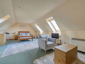 Ein gemütliches Schlafzimmer im Dachgeschoss mit einem Bett, einer Couch, einem Fernseher und einer hölzernen Truhe.