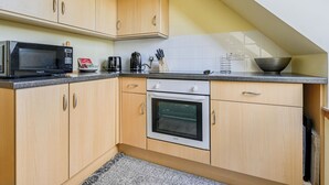 A kitchen with wooden cabinets, a microwave, a kettle, and an oven. - Bunloit Loft by Interhome (Drumnadrochit)
