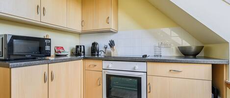 A kitchen with wooden cabinets, a microwave, a kettle, and an oven.