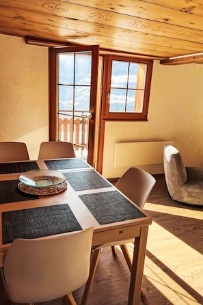 A wooden dining table with a glass centerpiece, surrounded by chairs, in a room with a wooden ceiling and a view through a window. - Charmant appartement dans chalet rénové by Interhome (Erschmatt)