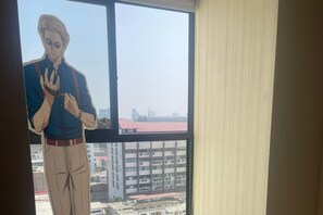 Ein Zimmer mit großem Fenster und Blick auf Gebäude, eine Person steht am Fenster.