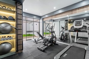Ein modernes Fitnessstudio mit Trainingsgeräten, Laufbändern und einem Wandgestell für Gewichte und Medizinbälle.