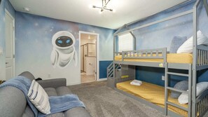 Ein Kinderzimmer mit Etagenbetten, einem grauen Sofa und einer Wandmalerei von einem Alien.