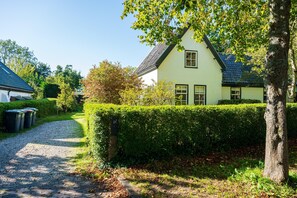 Une charmante maison avec une allée en gravier, entourée d’une végétation luxuriante et d’une haie bien entretenue.