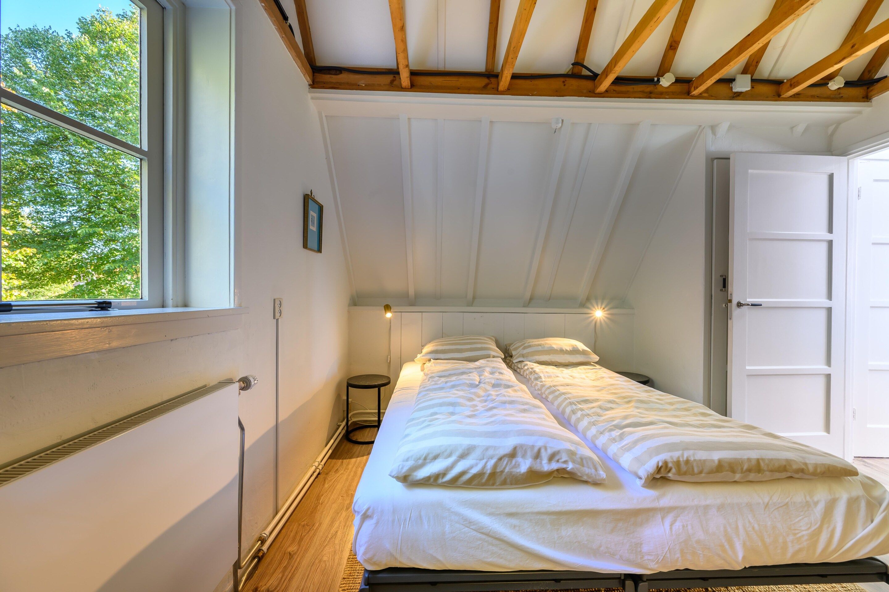 A single bed in a room with a sloped ceiling, a window, and a door.