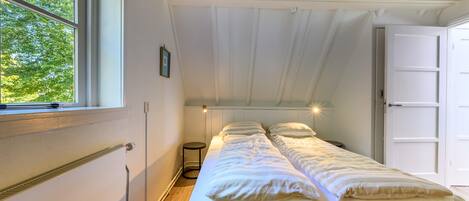 A single bed in a room with a sloped ceiling, a window, and a door.