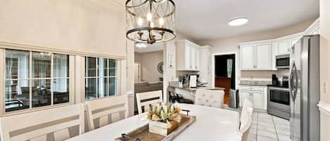 A modern kitchen with white cabinetry, a central island with a tray, and a chandelier.