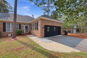 A two-story brick house with a front garage, a covered porch, and a well-maintained lawn. - Luxury Golf•Stay Simulator•Hot Tub•PGA Golden Tee (Pinehurst)