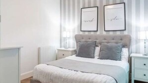 A bedroom with a bed, two bedside tables, a wall-mounted light fixture, and two framed pictures. - Charming 2 bed city garden flat in central Haymarket/ west end & parking (Edinburgh)