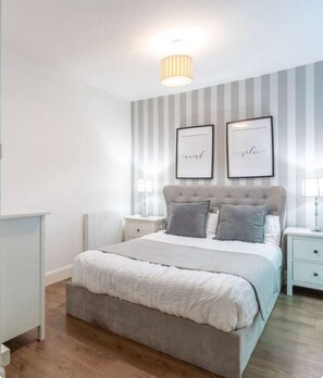 A bedroom with a bed, two bedside tables, a wall-mounted light fixture, and two framed pictures. - Charming 2 bed city garden flat in central Haymarket/ west end & parking (Edinburgh)