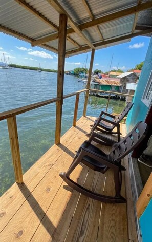 Eine Holzterrasse mit zwei Schaukelstühlen mit Blick auf ein Gewässer, im Hintergrund Boote und Häuser.