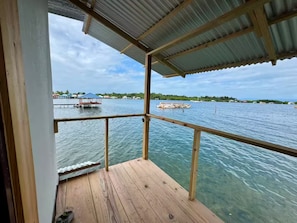 Eine Holzterrasse mit Metallveranda mit Blick auf ein Gewässer, auf dem Boote fahren, und eine ferne Küstenlinie.