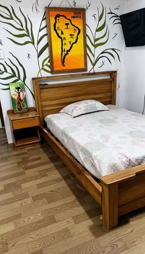 A wooden bed with a floral bedspread in a room with a wooden floor and a wall with a map of South America. - Heylie Tropical Retreat in Bocas del Toro, Panama (Isla Colon Bocas Del Toro)