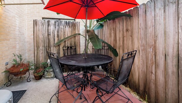 A patio with a round table and chairs, a red umbrella, and a wooden fence. - Near Hospitals 2 bedroom 1 bath in Baton Rouge (Baton Rouge)