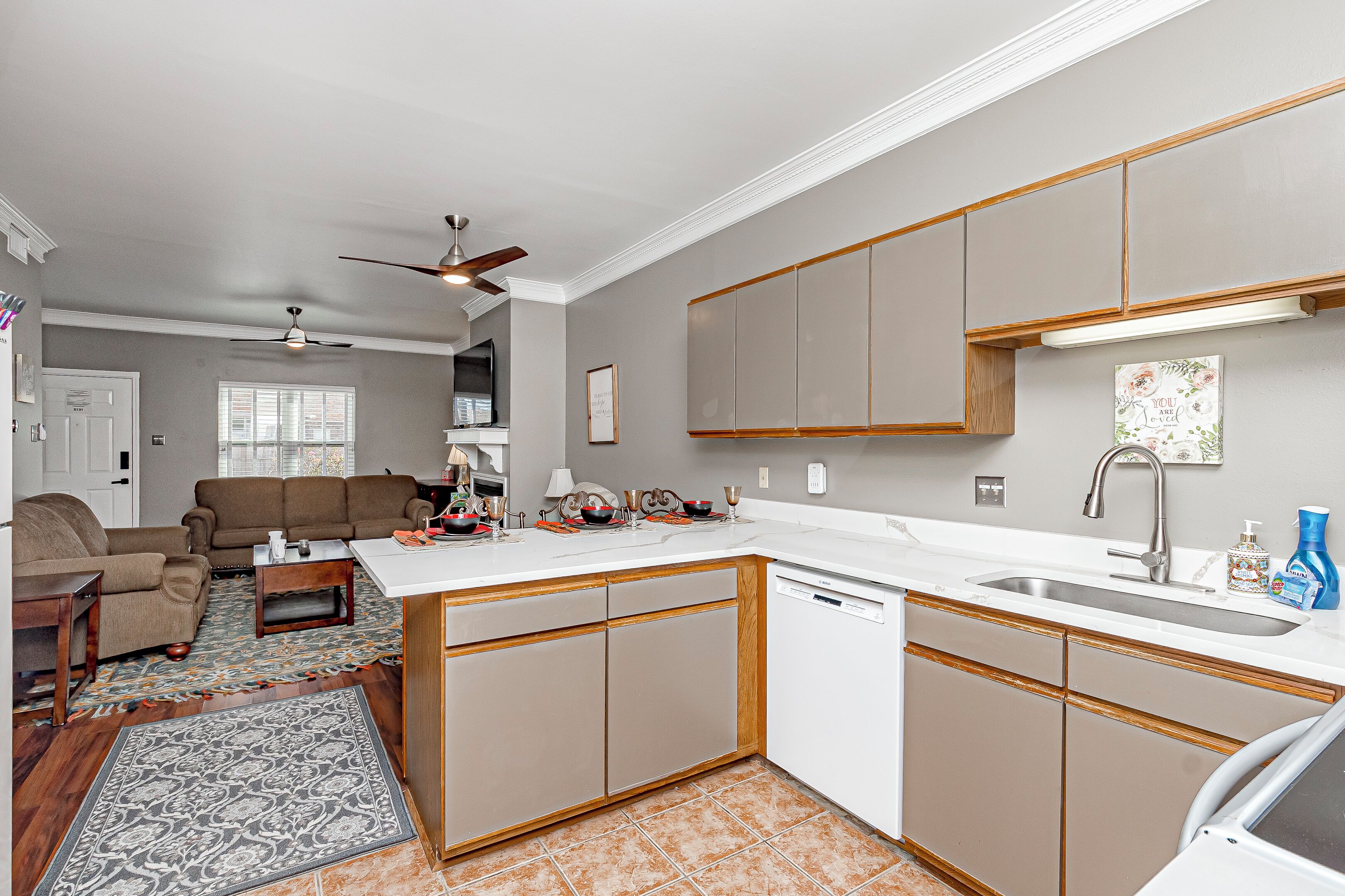 A compact kitchen with a dishwasher, a dining area with a sofa and table, and a ceiling fan.
