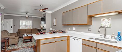 A compact kitchen with a dishwasher, a dining area with a sofa and table, and a ceiling fan.