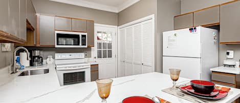 A modern kitchen with white appliances, wooden cabinets, and a dining area set with red plates and glasses.