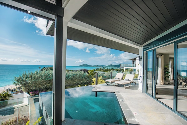 A modern outdoor pool area with clear blue water, lounge chairs, and a view of the ocean and distant mountains. - A Better Way to Stay! Oceanfront 2BR Villa with Private Pool and Antigua Views! (Urlings)