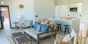 Un saló modern amb un sofà, una taula de centre i cadires. Hi ha una zona de cuina amb microones i tamborets.