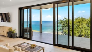 A modern living room with a large sliding glass door leading to a balcony with a view of the sea. - Ocean 20: Luxury 3-Bedroom Oceanfront Suite with Pool & Guest Cottage, Antigua (Urlings)