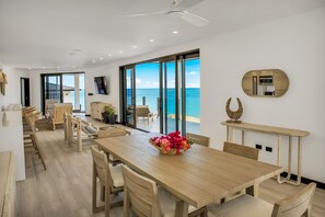 Un moderno comedor con una mesa de madera, sillas y un ventanal con vistas al océano.