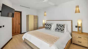 A modern bedroom with a large bed, wooden headboard, bedside lamps, a ceiling fan, and a TV mounted on the wall.