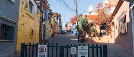 A narrow street with buildings on both sides, a gate with signs indicating no entry and speed limit, and a clear sky.