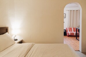 Ein Schlafzimmer mit Bett, Nachttisch und Blick auf einen anderen Raum durch einen Bogen.
