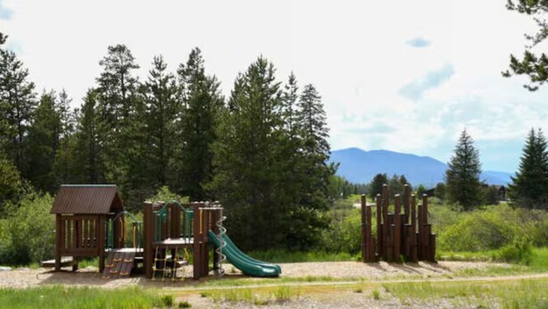 A playground with a slide and climbing structures, surrounded by trees and a mountain in the background. - Luxury 3 Bed Townhome • Walk to Town • on Ski Bus • Hot Tub • 2-Car Garage (Fraser)