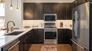 A modern kitchen with dark wood cabinets, stainless steel appliances, and pendant lighting. - Luxury 3 Bed Townhome • Walk to Town • on Ski Bus • Hot Tub • 2-Car Garage (Fraser)