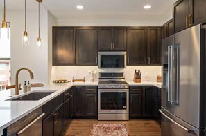 A modern kitchen with dark wood cabinets, stainless steel appliances, and pendant lighting. - Luxury 3 Bed Townhome • Walk to Town • on Ski Bus • Hot Tub • 2-Car Garage (Fraser)
