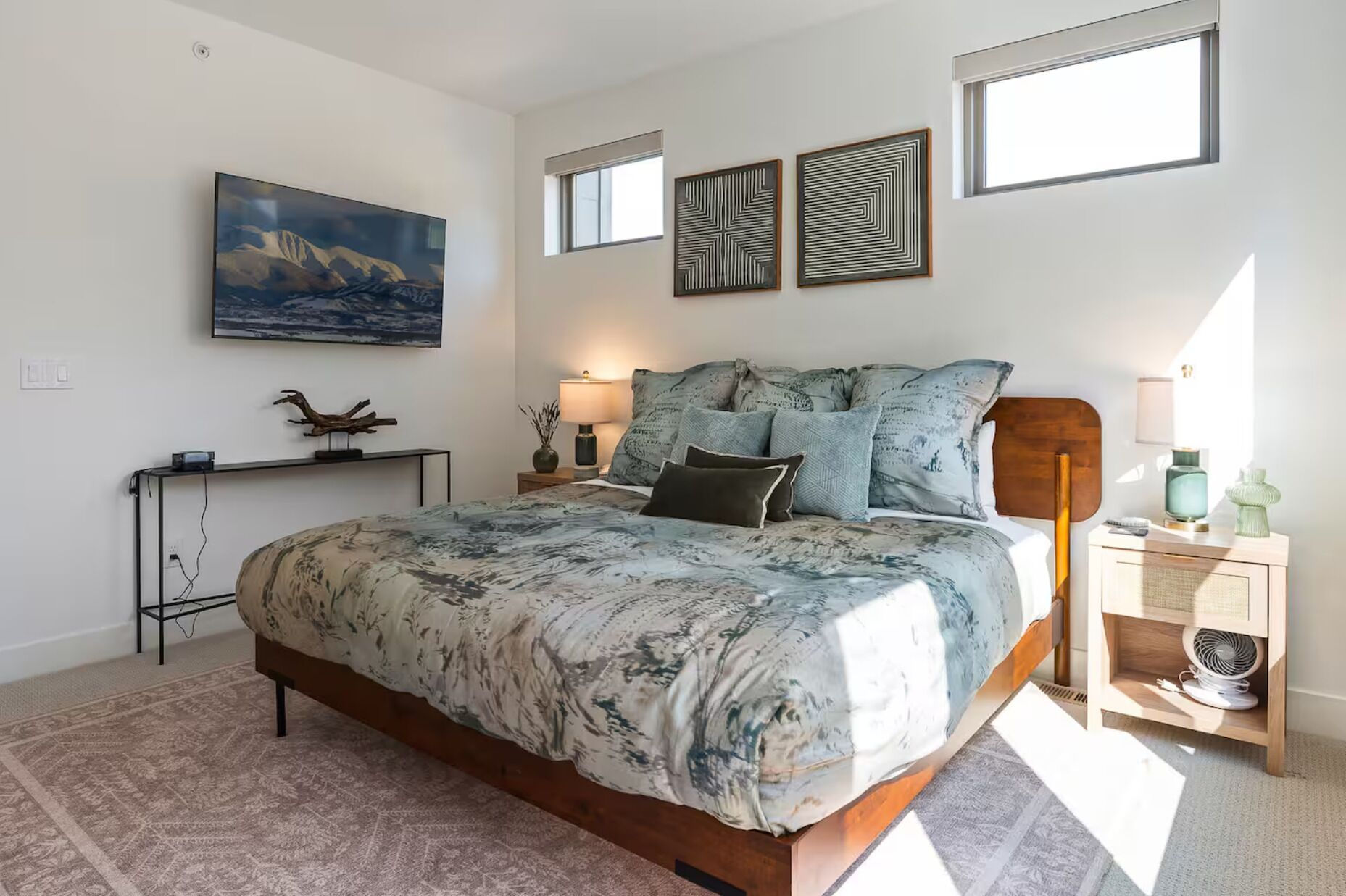 A bedroom with a large bed, a desk, and a nightstand. There are two windows and a painting on the wall.