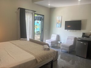 Habitación de hotel con cama, escritorio, silla, televisor y refrigerador.
