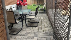 An outdoor patio with a table and chairs, a red umbrella, and a chain-link fence. - Tamunas Studio ,ideally for mid and long stay (Hamilton)