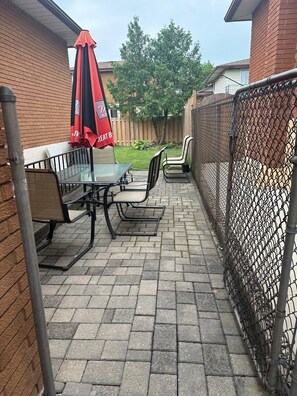 Eine Terrasse im Freien mit Tisch und Stühlen, einem roten Sonnenschirm und einem Maschendrahtzaun.