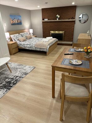 A modern bedroom with a bed, bedside tables, a fireplace, and a dining area with a table and chairs.
