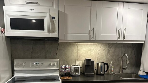 A kitchen with white cabinets, a microwave, a stove, and a sink. - Tamunas Studio ,ideally for mid and long stay (Hamilton)