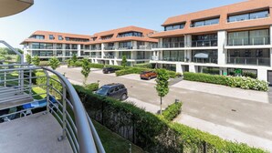 Un edificio residencial moderno de varios pisos con balcones, un estacionamiento y zonas verdes cuidadas.
