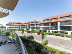A modern multi-story residential building with balconies, a parking area, and well-maintained greenery. - Goldsands III with parking by Interhome (De Haan)