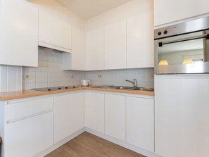 A modern kitchen with white cabinetry, a stainless steel oven, and a wooden countertop. - Goldsands III with parking by Interhome (De Haan)